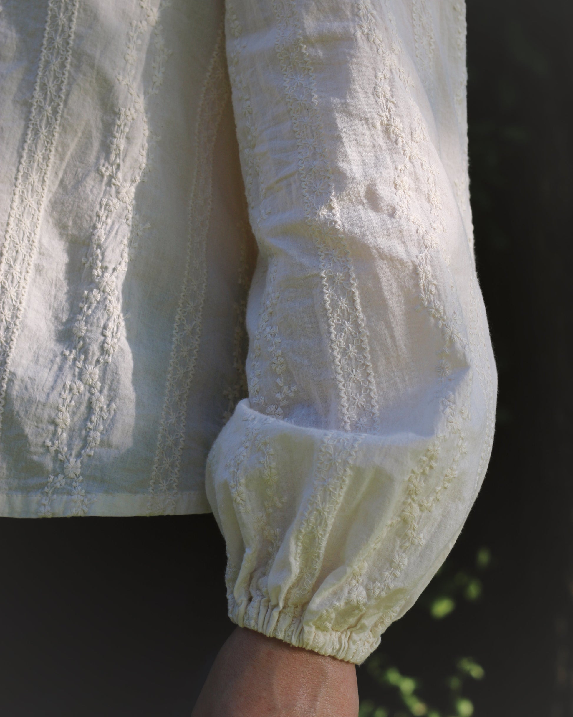 A close up image showing the sleeve of a embroidered ivory blouse. 
