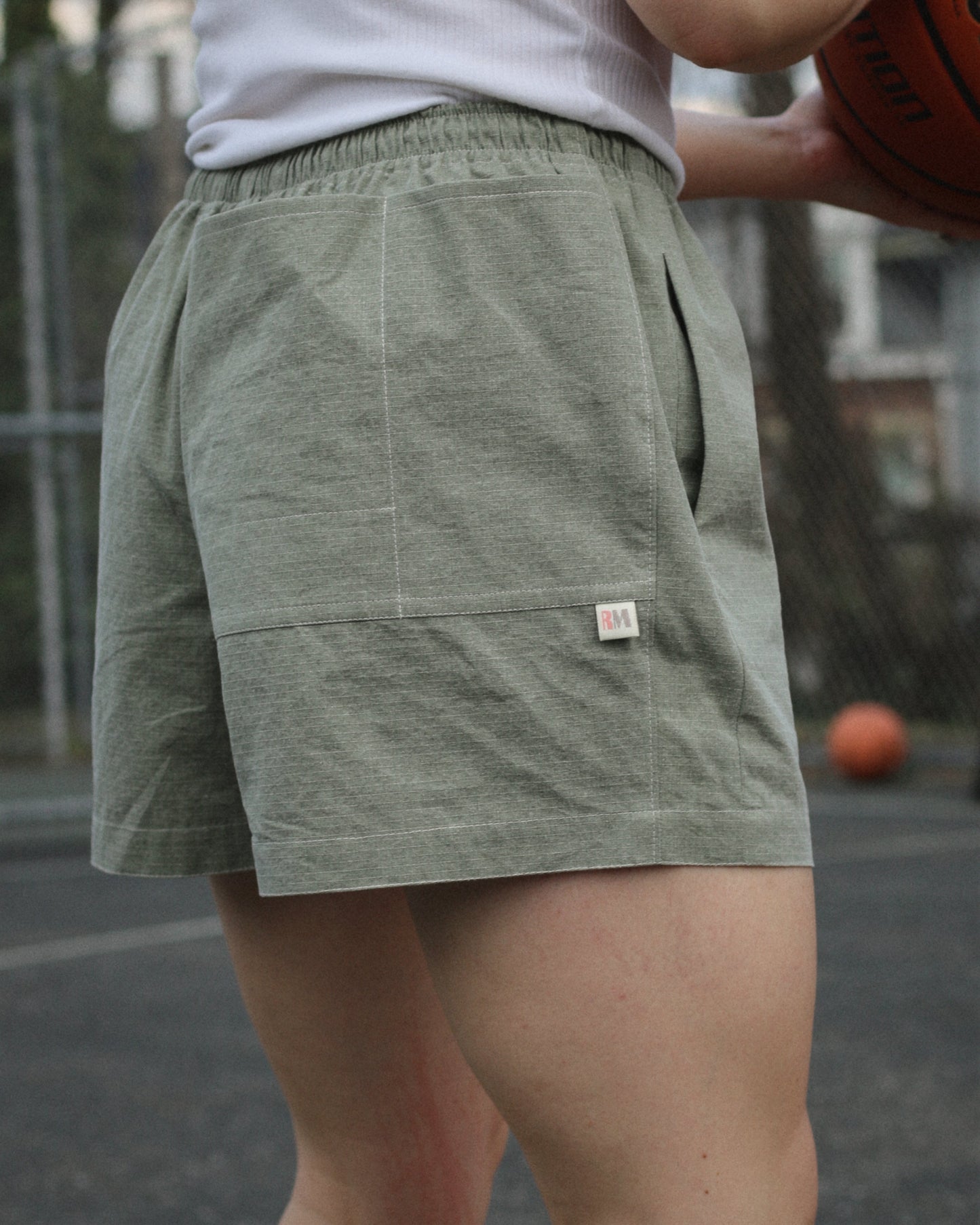 Women wearing green shorts with brand label and back pockets holding a basketball