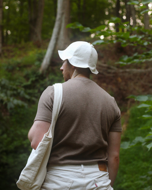 Person wearing a white cap and carrying a white bag in a forest setting